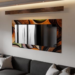 May include: Rectangular wall mirror with a decorative wooden frame featuring a pattern of brown, orange, and green organic shapes. The mirror is mounted on a light-colored wall above a dark gray sofa with white pillows.