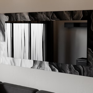 May include: A rectangular wall mirror with a decorative frame featuring a swirling black and white pattern. The mirror reflects a room with a window and a dark-colored shelf. The mirror is mounted on a white wall.
