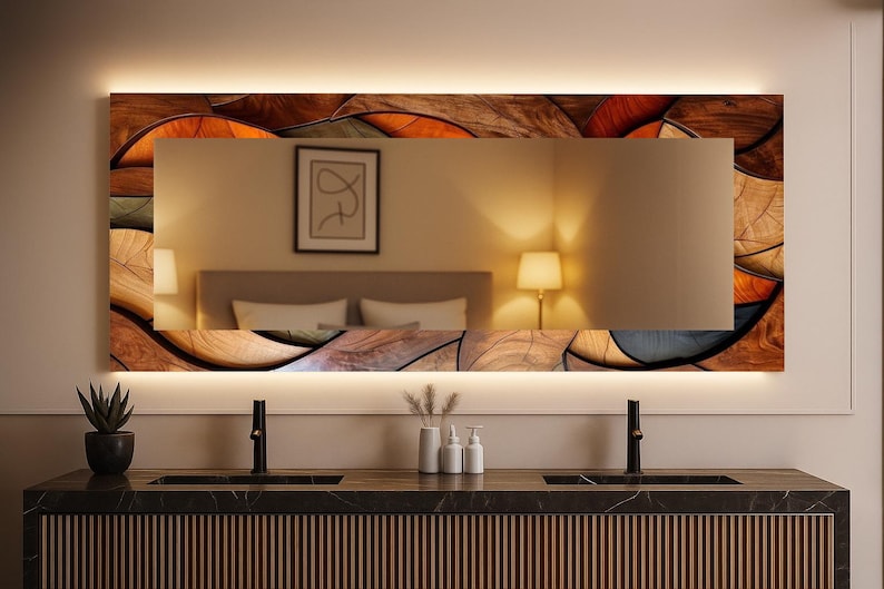 May include: Rectangular bathroom mirror with a decorative wooden frame featuring a mosaic of brown, orange, and gray shapes. The mirror has a built-in LED light and is mounted above a dark countertop with black faucets.