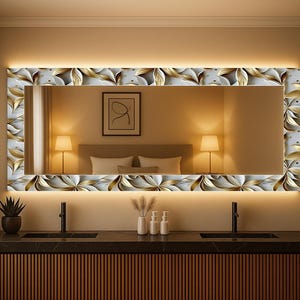 May include: A rectangular mirror with a floral pattern in gold and white, illuminated by warm lighting. It's mounted above a dark countertop with two black taps. The design suggests a modern bathroom setting, with a focus on decorative elements.