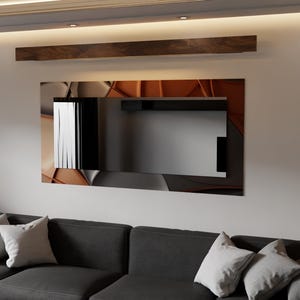 Può includere: Uno specchio da parete moderno con un design geometrico nei toni del marrone, grigio e nero. Lo specchio rettangolare è montato su una parete bianca sopra un divano grigio scuro con cuscini grigio chiaro. Una trave di legno è sopra lo specchio.