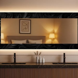 Könnte beinhalten: Ein rechteckiger Spiegel mit einem schwarzen floralen Rahmen und integrierter Beleuchtung. Der Spiegel ist über einem Badezimmerwaschtisch mit schwarzen Armaturen und einem Holzschrank montiert. Die Reflexion zeigt ein Schlafzimmer mit Bett und Lampen.