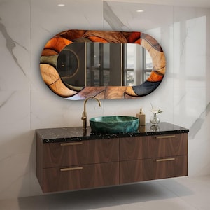 Puede incluir: Un espejo ovalado con un marco de madera decorativo en tonos marrón, naranja y gris cuelga sobre un tocador de madera oscura. Un lavabo de mármol verde y un grifo dorado completan la configuración del baño. El tocador tiene cuatro cajones con manijas doradas.
