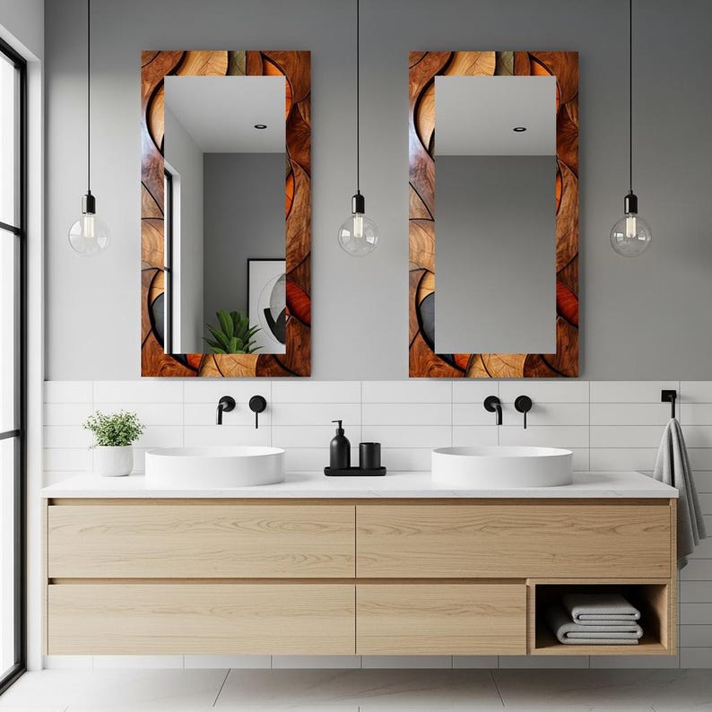 May include: Two rectangular mirrors with decorative wooden frames hang above a light wood vanity with two white sinks. The mirror frames feature a mosaic design with brown, orange, and black elements. The bathroom has a modern design.