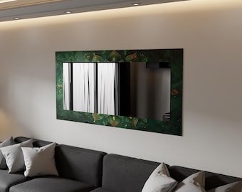 Op de afbeelding: Een rechthoekige wandspiegel met een donkergroene lijst met gouden bladaccenten. De spiegel reflecteert verticale witte en zwarte lijnen. De spiegel is gemonteerd op een lichtgekleurde muur boven een donkergrijze bank met grijze kussens.