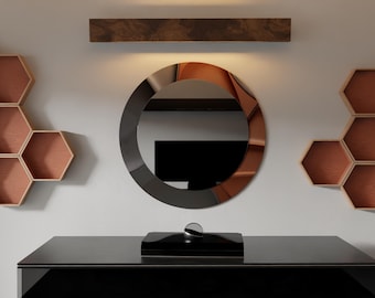 May include: A modern interior design featuring a black dresser with a decorative box and a clear orb. A large circular mirror with a dark frame hangs above the dresser. Honeycomb-shaped shelves and a wooden shelf are mounted on the wall.