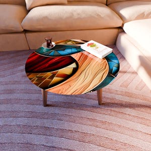 May include: A round coffee table with a colorful, abstract design. The tabletop features a mosaic of red, blue, and wood-grain patterns. The table has three wooden legs and a book with flowers on top.