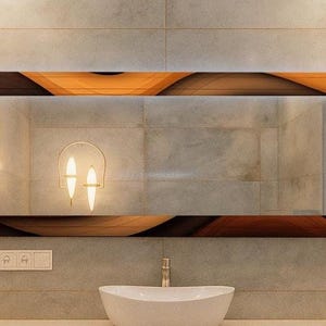 May include: A rectangular bathroom mirror with a decorative wooden frame in brown and orange tones. Two sconces with lampshades flank the mirror. A white sink and tap are below the mirror.