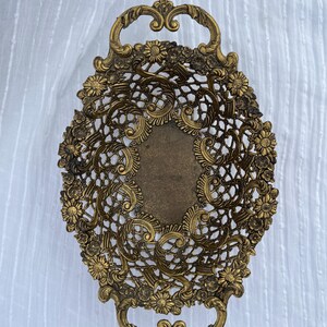 May include: An antique brass oval tray with ornate floral and openwork lace design. The tray features two curved handles and a central rectangular area. The brass has a warm, aged patina, suggesting vintage craftsmanship. The tray is suitable for decorative purposes.