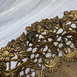 May include: Close-up of a decorative, antique-style tray with intricate floral and scrollwork details. The tray is made of a gold-toned metal and features a lattice design. The edges are adorned with detailed flowers and leaves.