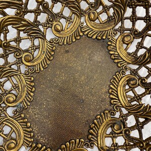 May include: Ornate, antique-style metal basket with a gold finish. The basket features a detailed openwork design with scrolling leaf and floral motifs. The center has a textured, solid surface. The overall aesthetic is vintage and decorative.