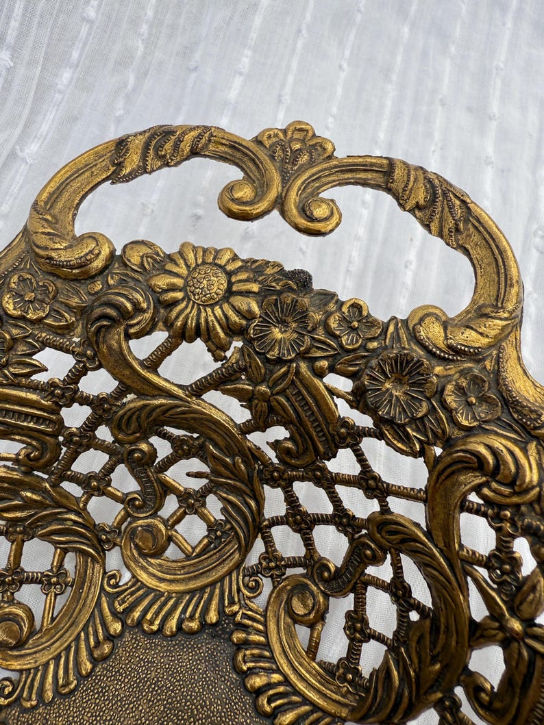 May include: Ornate gold-colored metal tray with a floral and scroll design. The tray features a handle and intricate openwork detailing, including flowers and a lattice pattern. The overall aesthetic is vintage and decorative.