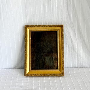 May include: An ornate gold picture frame with a dark interior. The rectangular frame features detailed carvings and a glossy finish. The empty frame is ready to display a photograph or artwork. It is set against a white background.