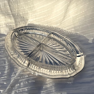 May include: An oval, divided serving dish with a clear glass interior and a silver-coloured metal rim. The dish is divided into four sections and features a starburst design in the centre.