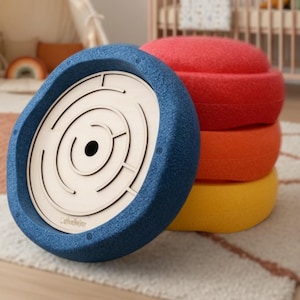 Può includere: Un gioco labirinto blu con interno in legno chiaro e bordo strutturato blu scuro. Dietro, tre cuscini rotondi colorati in rosso, arancione e giallo. Gli oggetti sono su un tappeto fantasia.