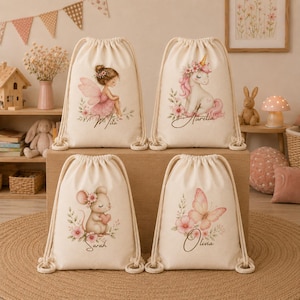 May include: Four off-white canvas drawstring backpacks featuring printed illustrations of a fairy, a unicorn, a mouse, and a butterfly, each surrounded by floral accents. The names Mita, Aurelia, Sarah, and Olivia are printed below the designs.