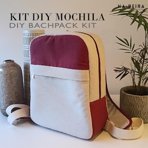 Op de afbeelding: Een doe-het-zelf rugzakkits met een bordeauxrode bovenkant, een gebroken witte body en crèmekleurige bandjes. De rugzak heeft een ritsvak en een crèmekleurige band. De tekst op de afbeelding luidt "KIT DIY MOCHILA DIY BACHPACK KIT".