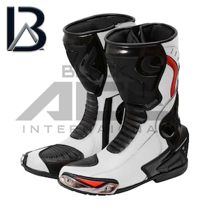 Puede incluir: Par de botas de moto blancas y negras con detalles rojos. Las botas tienen un diseño de caña alta con paneles protectores y una puntera metálica. El logotipo "B A INTERNATIONAL" es visible.