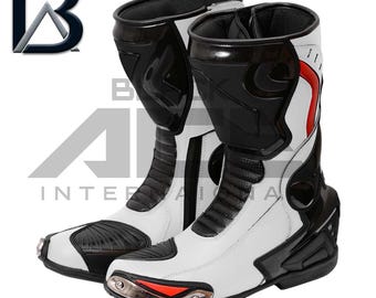 May include: Pair of white and black motorcycle boots with red accents. The boots have a high-top design with protective panels and a metallic toe cap. The boots have the logo "B A INTERNATIONAL" in the upper left corner.