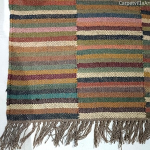 Op de afbeelding: Een rechthoekig tapijt met een gestreept patroon in verschillende kleuren, waaronder bruin, groen en rood. Het tapijt heeft een gefranjerde rand en de tekst "CarpetvillaArt" in de rechterbovenhoek.