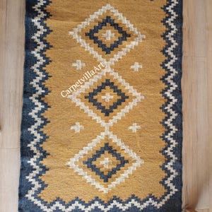May include: Mustard yellow and navy blue rectangular rug with a geometric diamond pattern. The rug features a central design of three diamond shapes with white and navy blue accents. The border is navy blue with a zigzag pattern. The text "CarpetvillaArt" is visible.