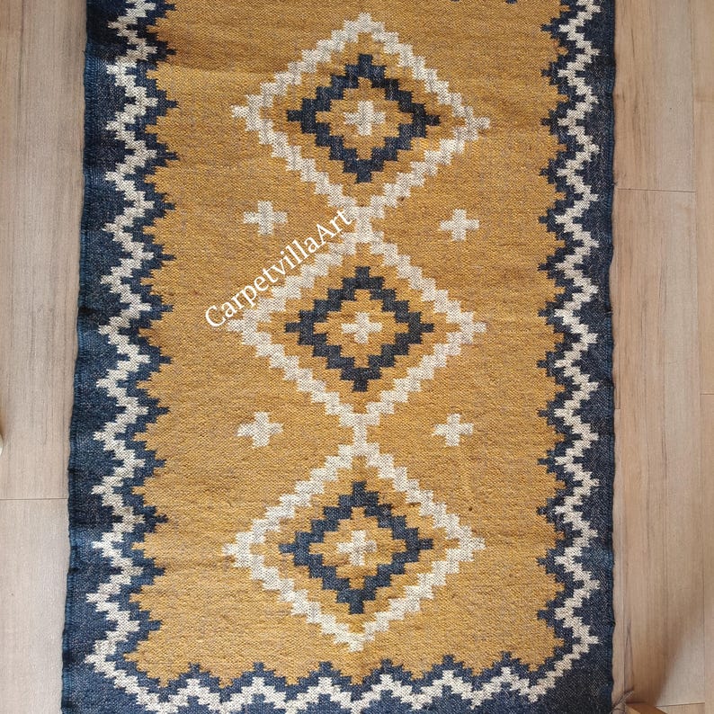 May include: Mustard yellow and navy blue rectangular rug with a geometric diamond pattern. The rug features a central design of three diamond shapes with white and navy blue accents. The border is navy blue with a zigzag pattern. The text "CarpetvillaArt" is visible.