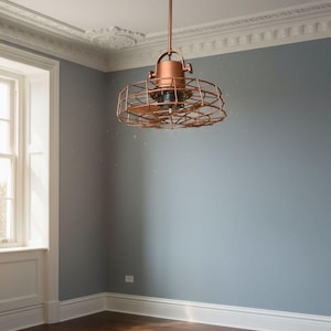 Pode incluir: Um ventilador de teto cor de cobre com um design em forma de gaiola pende do teto. O ventilador é suspenso por uma haste de cobre e é montado em um medalhão de teto branco. A sala tem paredes cinzentas e piso de madeira escura.
