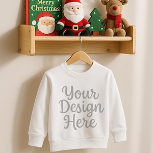 クリスマス スウェットシャツ モックアップ | 子供用ホリデー ジャンパー PNG | ハンガーに掛けた白いクルーネック スウェットシャツ | 幼児用サンタ ホリデー シェルフ シーン モックアップ