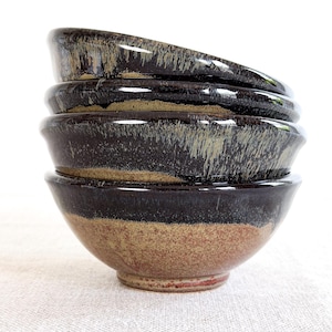 May include: A stack of four ceramic bowls. The bowls have a dark brown glaze on the top half, transitioning to a tan and reddish-brown base. The bowls are stacked on top of each other.