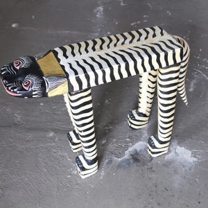 May include: A hand-painted wooden zebra sculpture with black and white stripes. The zebra has a black head with red accents and is designed to be a decorative piece. The sculpture is a unique home decor item.