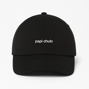 Puede incluir: Gorra de béisbol negra con el texto blanco "papi chulo". La gorra tiene una visera curva y un botón en la parte superior. El sombrero está hecho de un material suave.