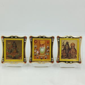 Könnte beinhalten: Drei gerahmte religiöse Bilder mit goldenen Rändern und Schmuckakzenten. Die Bilder zeigen Gottheiten und religiöse Figuren. Jeder Rahmen steht auf einem transparenten Kunststoffständer.