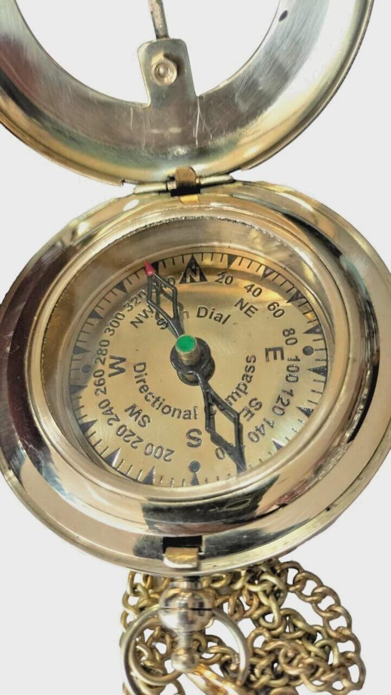 Puede incluir: Una br&uacute;jula de lat&oacute;n vintage con tapa con bisagras y cadena. La esfera de la br&uacute;jula presenta marcas direccionales, una aguja y las palabras "Directional Compass" y "Dial". La br&uacute;jula es una herramienta de navegaci&oacute;n cl&aacute;sica.