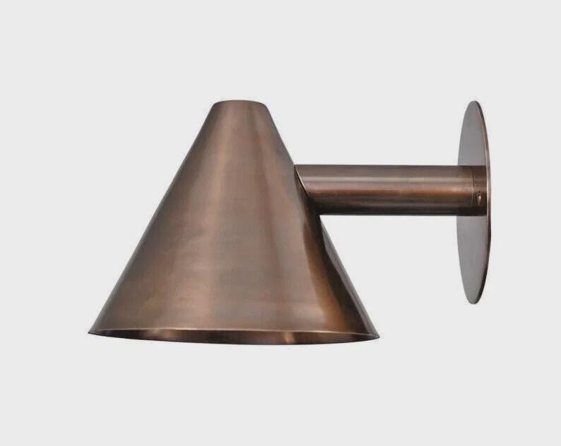 May include: A bronze-colored wall sconce with a conical shade and a cylindrical arm. The sconce has a circular mounting plate. The metal fixture is designed for indoor or outdoor lighting.