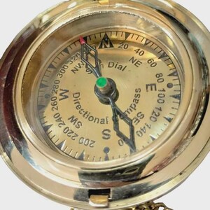 Puede incluir: Una br&uacute;jula de lat&oacute;n vintage con tapa con bisagras y cadena. La esfera de la br&uacute;jula presenta marcas direccionales, indicadores de grados y la palabra "Dial". La aguja apunta hacia el norte. Una herramienta de navegaci&oacute;n cl&aacute;sica.