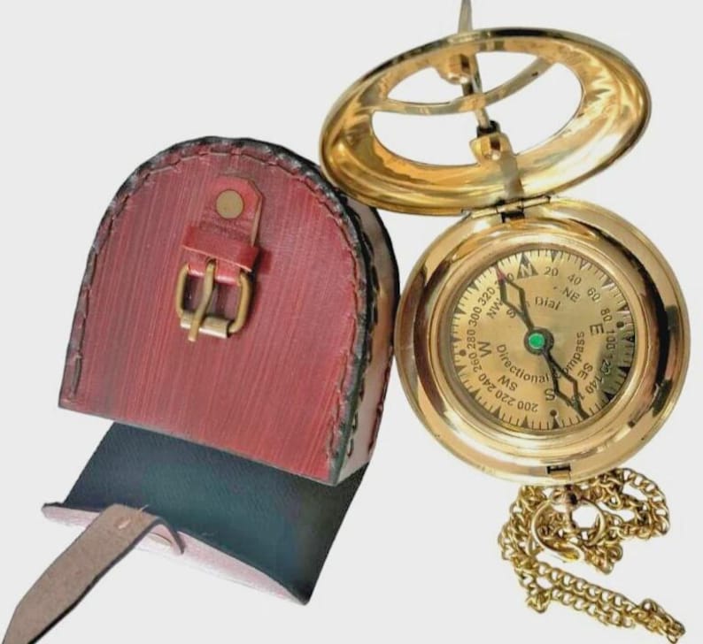 Puede incluir: Una br&uacute;jula de sol de lat&oacute;n vintage con una funda de cuero. La br&uacute;jula presenta una esfera detallada con marcas direccionales y una cadena. La funda de cuero rojo tiene un cierre de hebilla. Una herramienta de navegaci&oacute;n cl&aacute;sica.