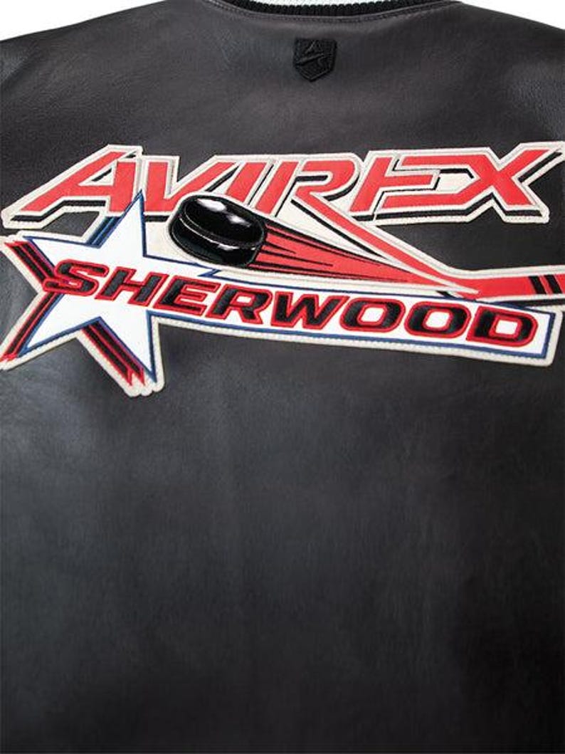 May include: Black leather jacket with a hockey-themed patch. The patch features the word "AVIREX" in red and white, a hockey puck, and the word "SHERWOOD" in red and white. A small logo is at the top.