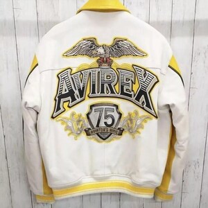 May include: White and yellow bomber jacket with the text "AVIREX" and "75 AVIATOR'S KING" on the back. The jacket features an eagle graphic with a crown. Yellow accents are on the collar, sleeves, and hem. The jacket is made of a smooth material.