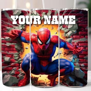May include: A stainless steel tumbler featuring a vibrant illustration of Spider-Man breaking through a brick wall. The design includes the text "YOUR NAME" in bold white letters. The tumbler has a straw.