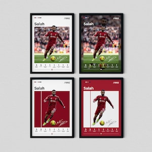 Puede incluir: Cuatro pósteres enmarcados que muestran a Mohamed Salah con un uniforme de fútbol rojo. Dos pósteres lo muestran en un campo con público, mientras que dos lo muestran sobre un fondo rojo o blanco sólido. Cada uno incluye el texto Salah, /1992.