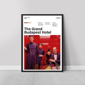 Puede incluir: Un póster enmarcado de la película "El Gran Hotel Budapest" con una foto del elenco. El póster tiene un marco negro y un fondo blanco con el título y los créditos de la película. La imagen incluye una paleta de colores y el año 2014.