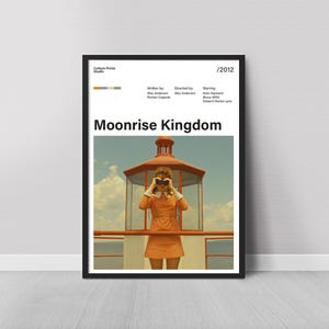 Puede incluir: Póster enmarcado de la película "Moonrise Kingdom", con una persona con un vestido naranja usando binoculares. El póster tiene un marco negro y se muestra contra una pared blanca.