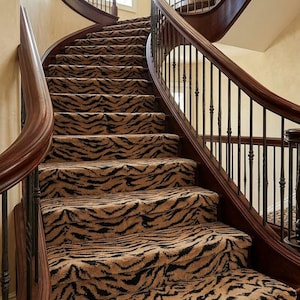 May include: A curved staircase with a tiger stripe patterned carpet. The stairs have dark wood railings and balusters. The walls are a light beige color, and a window is visible at the top of the stairs.