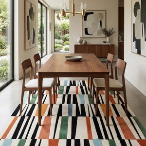 May include: A rectangular area rug featuring a geometric pattern of vertical stripes in black, white, burnt orange, forest green, and light blue. The rug is positioned under a wooden dining table with four matching chairs with white seats.