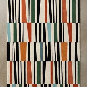 May include: A rectangular area rug featuring a repeating geometric pattern of vertical black lines on an off-white background, interspersed with solid, trapezoidal blocks of color in burnt orange, forest green, and light blue throughout.