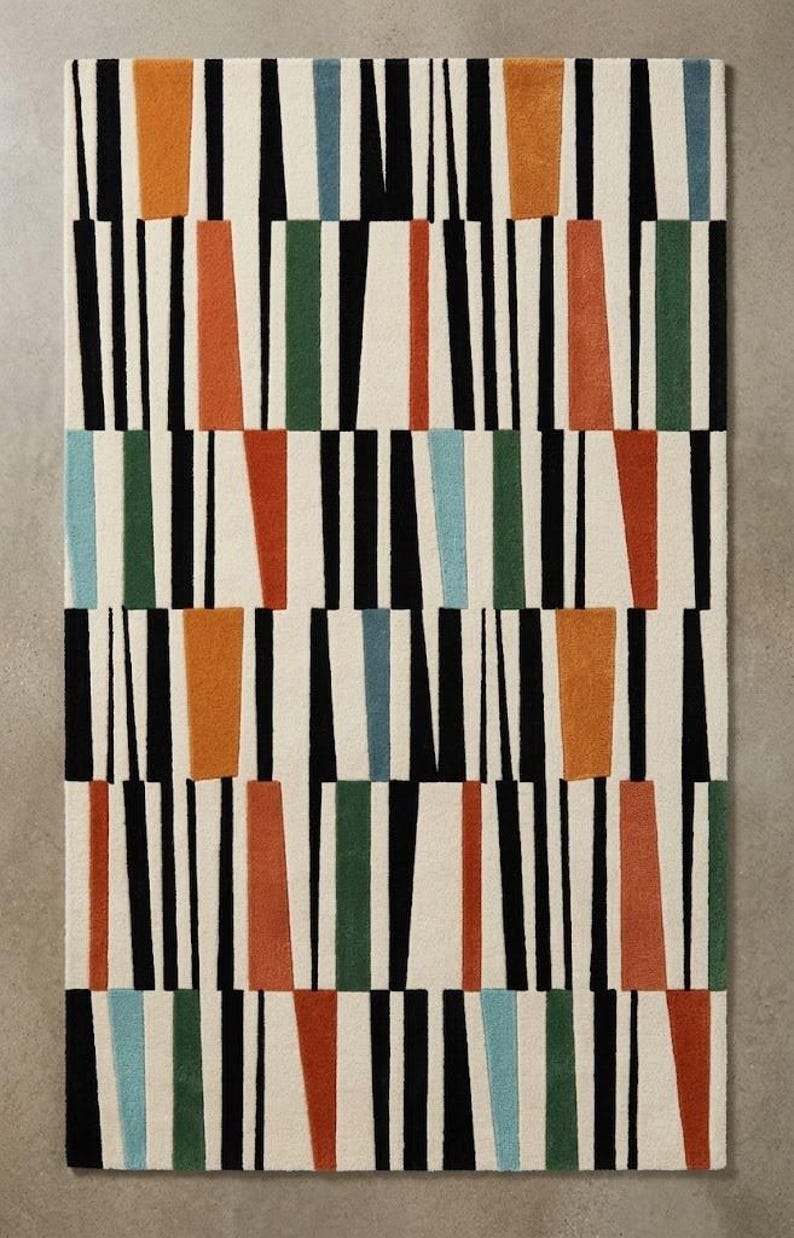 May include: A rectangular area rug featuring a repeating geometric pattern of vertical black lines on an off-white background, interspersed with solid, trapezoidal blocks of color in burnt orange, forest green, and light blue throughout.