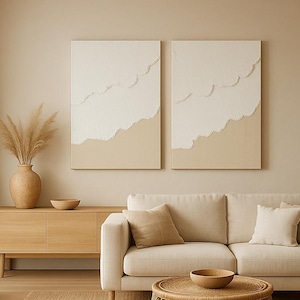 Puede incluir: Salón de tonos neutros con un sofá beige, una mesa de centro redonda de mimbre y un mueble de madera. Dos obras de arte abstractas cuelgan sobre el sofá. Una lámpara colgante de mimbre y plantas en macetas completan el ambiente natural.