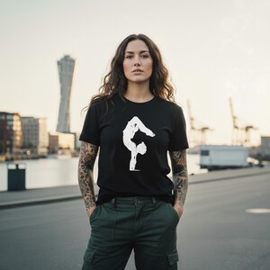 May include: A black short-sleeved t-shirt featuring a white graphic print of a person performing a handstand. The shirt has a crew neckline and a straight hem, constructed from a solid black fabric with a contrasting white silhouette design.