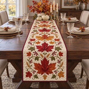 May include: A rectangular table runner featuring a cream-colored fabric base with an embroidered pattern of vibrant red, orange, and green maple leaves, wheat stalks, and small red berries, finished with a dark red border and quilted texture.