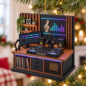 Puede incluir: Un adorno colgante rectangular que muestra un estudio de DJ en miniatura con una consola de mezclas etiquetada como DJ WILLIAM, un monitor, auriculares, altavoces y un micrófono. Incluye estantes de madera con plantas y un mueble de almacenamiento.